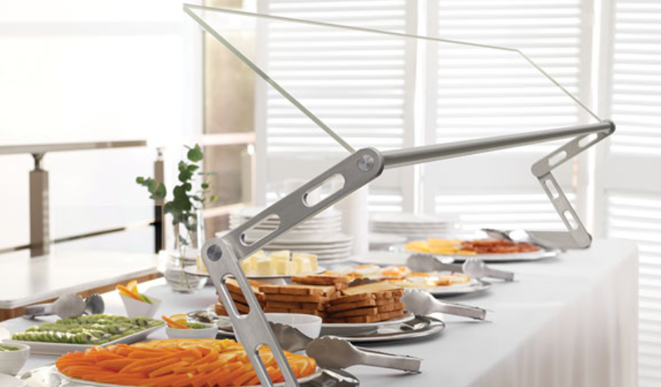 An angled glass sneeze guard over a breakfast buffet.